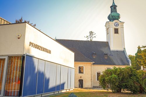 Eine Kirche mit einem Glockenturm und einem modernen Gebäude mit der Aufschrift Pfarrzentrum.