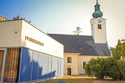 Eine Kirche mit einem Glockenturm und einem modernen Gebäude mit der Aufschrift Pfarrzentrum.