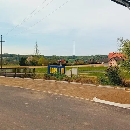 Eine leere Straße mit einem Schild, auf dem Dorp steht. Dahinter befindet sich ein breites Feld mit einigen Häusern und einem Zaun.