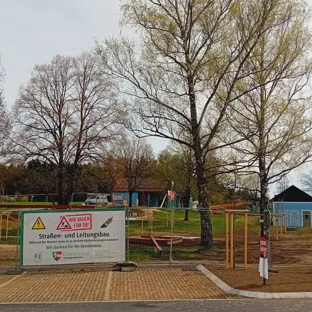 Baustelle mit Bäumen und einem Warnschild. Das Schild warnt vor dem Betreten und unterirdischen Kabeln und Versorgungsleitungen.