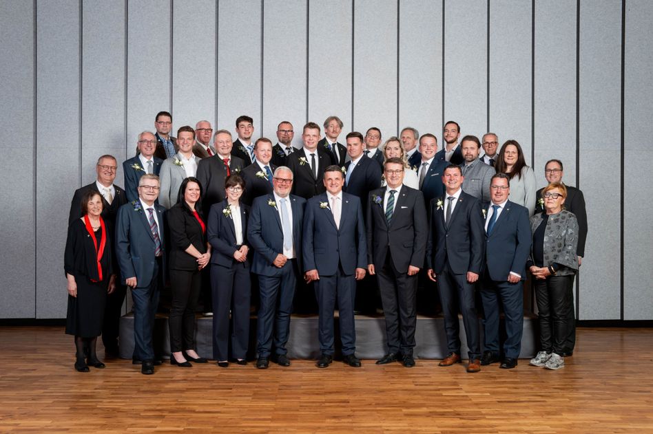 Eine Gruppe von Männern und Frauen in formeller Kleidung, die vor einer grauen Wand stehen.