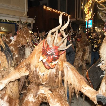 Eine Gruppe von Menschen in Hörnerkostümen mit Masken, vermutlich für ein Fest, geht nachts auf der Straße.