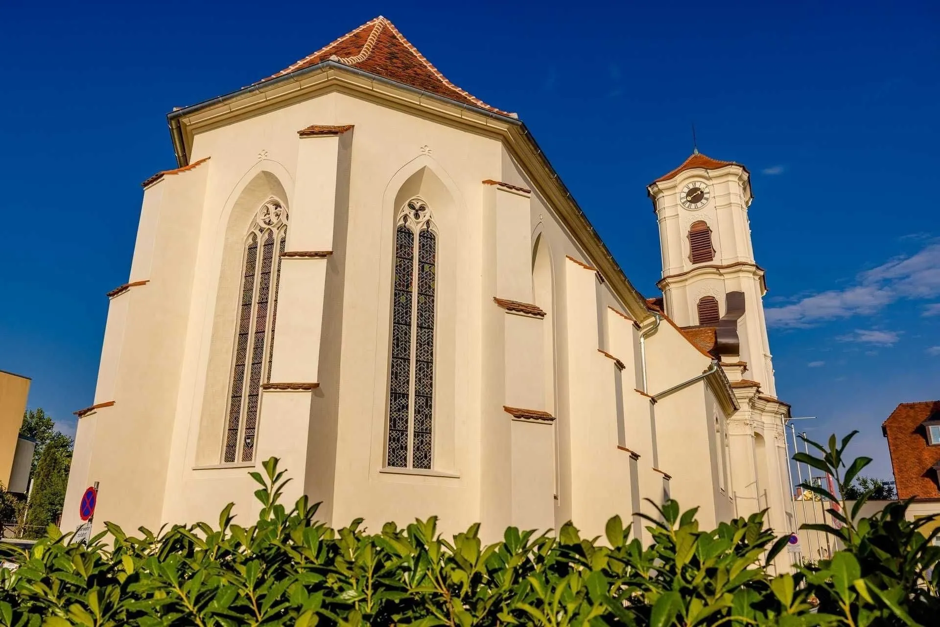 A white church with a brown roof, two arched windows, and a tower with a clock under a clear blue sky.
