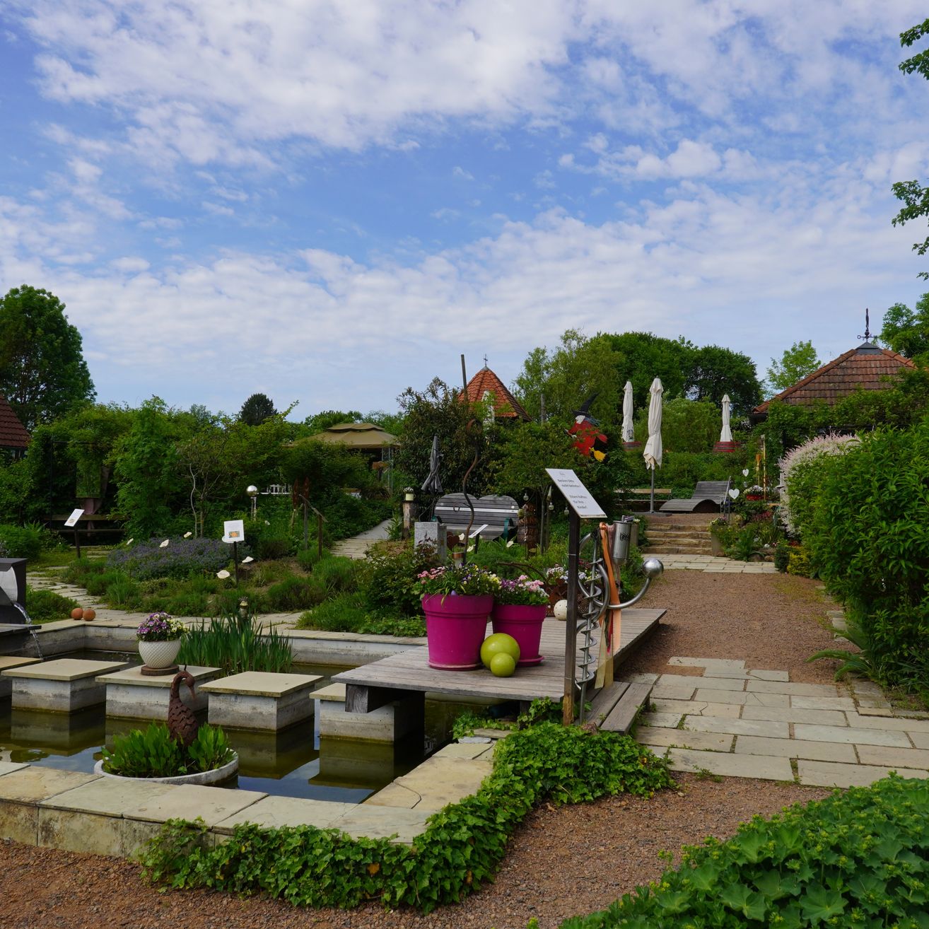 Outdoor garden with trees, plants, and a pond, with a sign on a wooden deck.