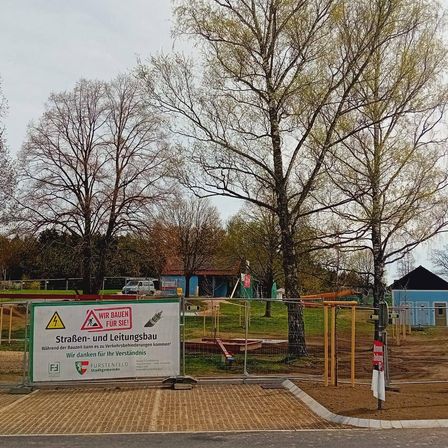 Construction site with trees and a sign warning against entering. The sign includes a warning about underground cables and utilities.