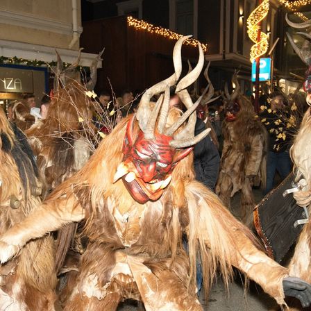 A group of people dressed in horned costumes with masks, possibly for a festival, walking in the street at night.