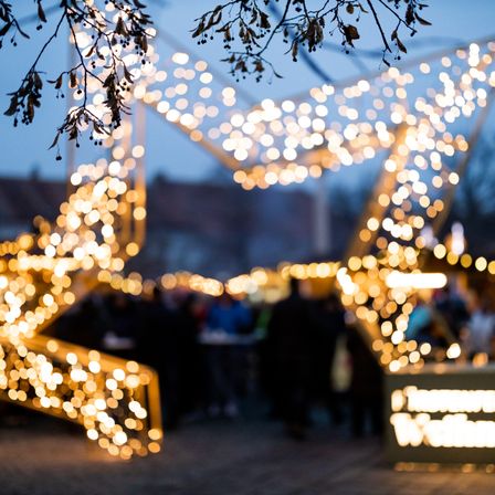 A close up of a Christmas star made of lights, with a crowd of people in the background.