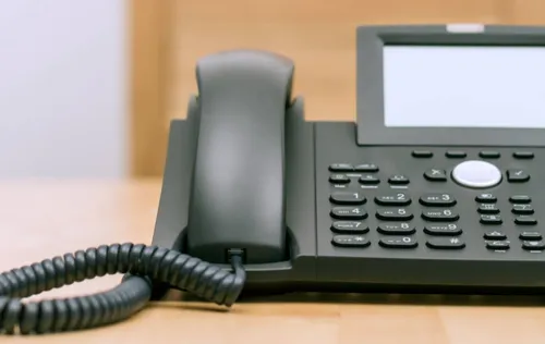 Ein schwarzer Bürotelefon mit digitalem Bildschirm und Nummerntasten steht auf einem Holzschreibtisch.
