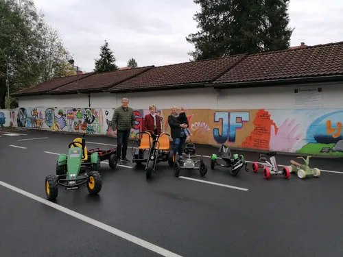 Drei Erwachsene und ein Kind posieren vor einem Gebäude mit Graffiti und mehreren Pedalautos.