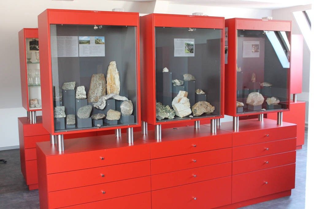 Drei rote Vitrinen mit verschiedenen Steinen und Mineralien sind auf einem roten Schrank mit Schubladen platziert.