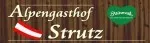 Das Bild zeigt das Logo für Alpengasthof Strutz, ein Restaurant oder Gasthof, auf einem hölzernen Hintergrund. Es enthält ein grünes Blattlogo, die österreichische Flagge und ein stilisiertes Textdesign.