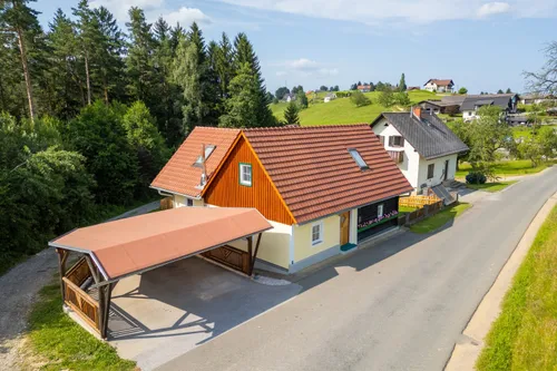 Ein Luftbild eines Hauses mit rotem Dach und Carport, umgeben von einem grünen Rasen und Bäumen.