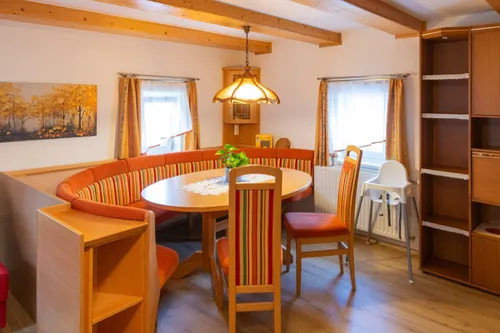 Ein Essbereich mit einem runden Tisch und vier Stühlen, geschmückt mit einer Pflanze. Der Raum verfügt über Holzbalken an der Decke, Holzböden und einen Heizkörper in der Nähe der Fenster.