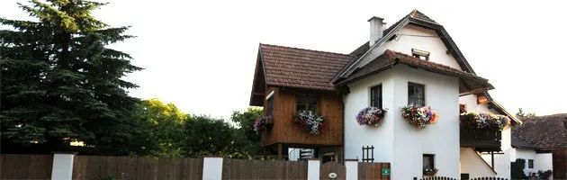 Ein charmantes weißes Haus mit braunen Akzenten, geschmückt mit Blumenkästen an den Fenstern und umgeben von einem Holzzaun und Grün.