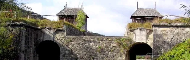 Eine alte Steinbrücke mit zwei kleinen Holzhäusern auf der Spitze, jedes mit einem moosbedeckten Dach und einem Zaun davor.