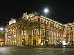 Das Wiener Staatsopernhaus ist bei Nacht beleuchtet und zeigt seine großartige Architektur mit zahlreichen Fenstern und einer prominenten Straßenlaterne davor.
