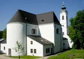 Eine große weiße Kirche mit schwarzem Dach und einem hohen Glockenturm, umgeben von grünem Gras und Bäumen.
