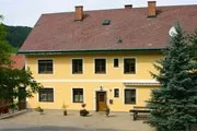 Ein gelbes Haus mit rotem Dach und mehreren Fenstern, umgeben von Bäumen und einer Bank davor.