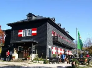 Ein großes schwarzes Gebäude mit rot-weiß gestreiften Fensterläden und einer Flagge davor, mit Menschen, die draußen in der Nähe von Topfpflanzen stehen und einem klaren blauen Himmel im Hintergrund.