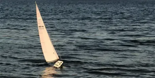 Ein weißer Segelboot mit der Aufschrift 'IBS-95' und '26-81' auf seinem Segel segelt in der Mitte des Meeres mit Wellen.