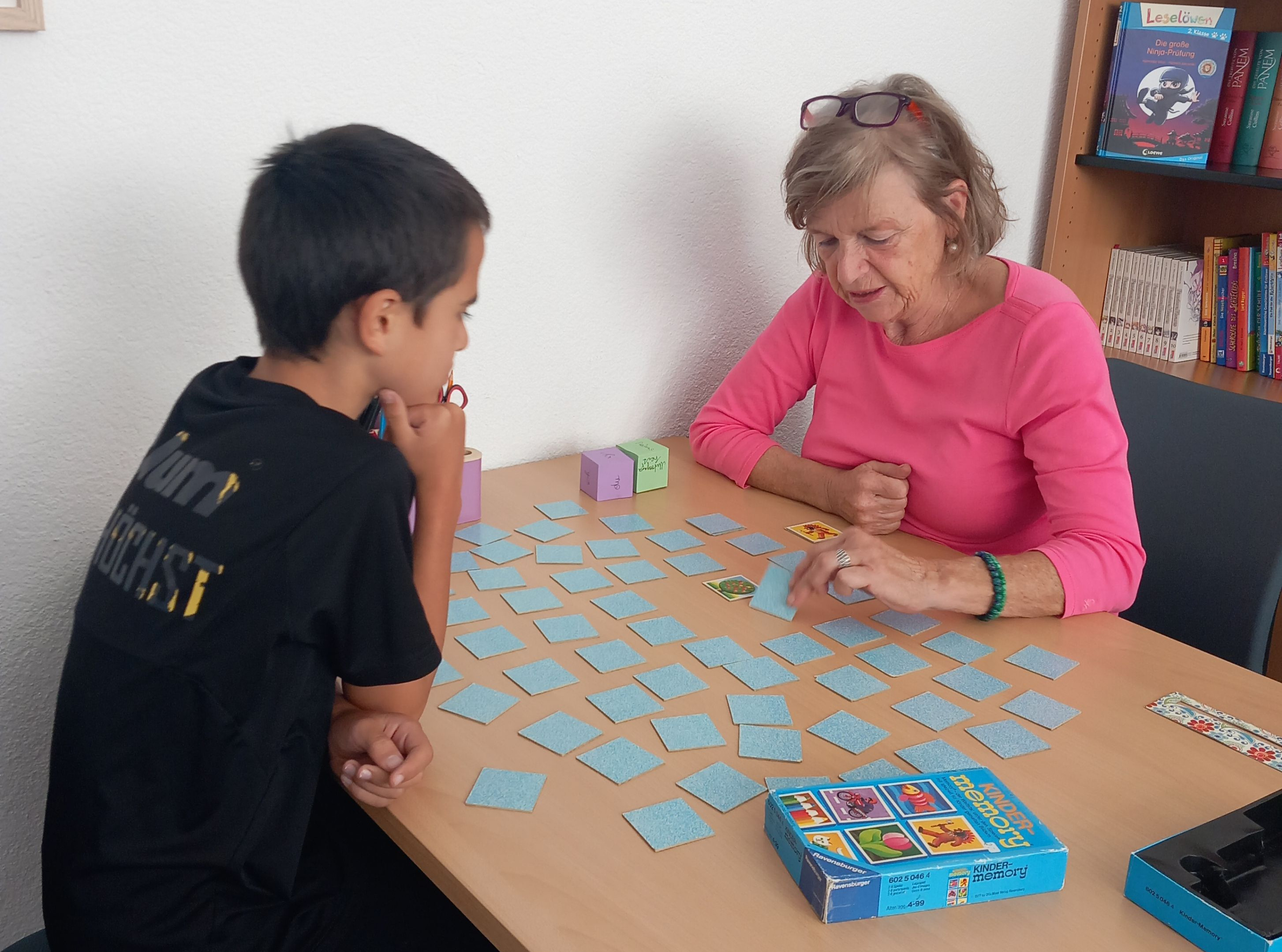Eine ältere Frau und ein junger Junge spielen ein Gedächtnisspiel auf einem Tisch.