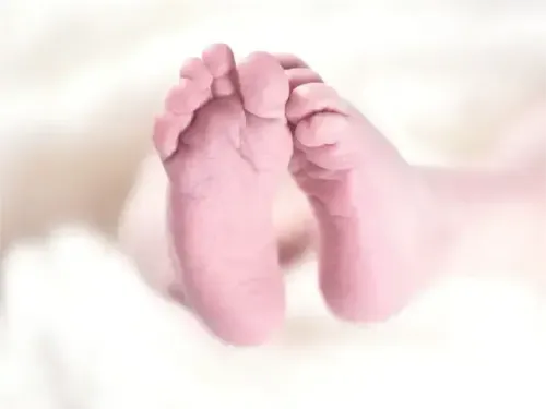 Eine Nahaufnahme der Füße eines Neugeborenen, die auf einer weißen Decke liegen und zarte Haut und winzige Zehen zeigen.