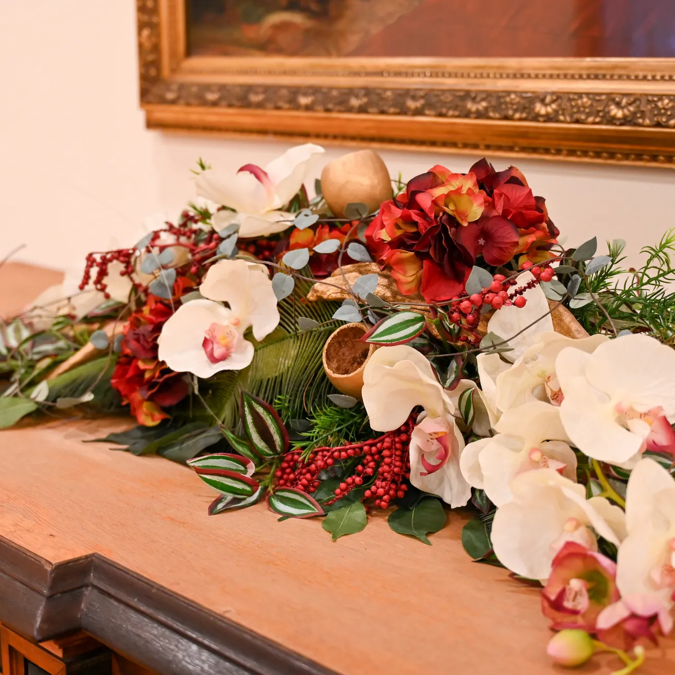 Eine Blumenarrangement mit weißen und roten Blumen, grünen Blättern und Beeren auf einer Holzoberfläche.