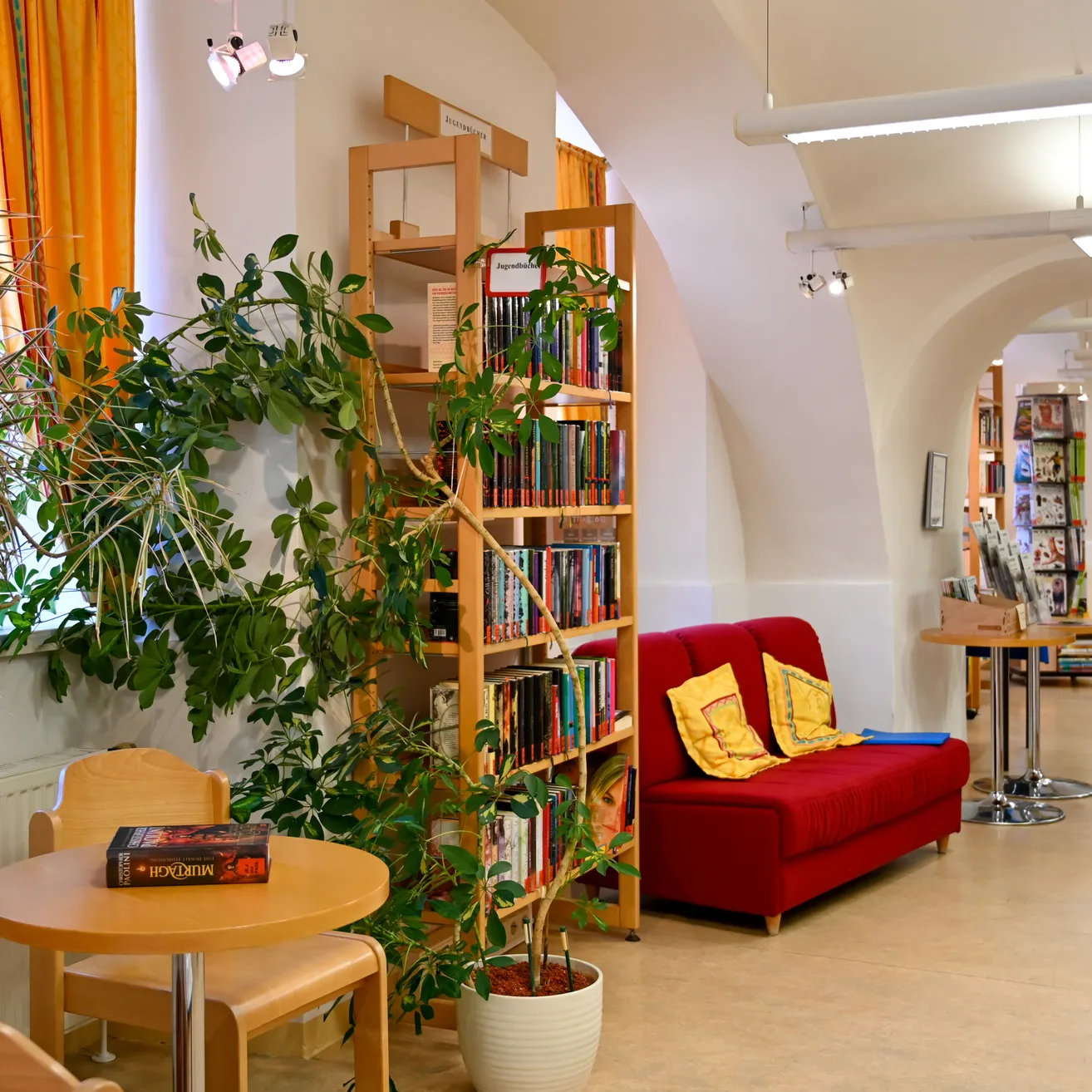 Ein gemütlicher Lesebereich mit einem roten Sofa, einem Holztisch und einem mit Büchern gefüllten Bücherregal.