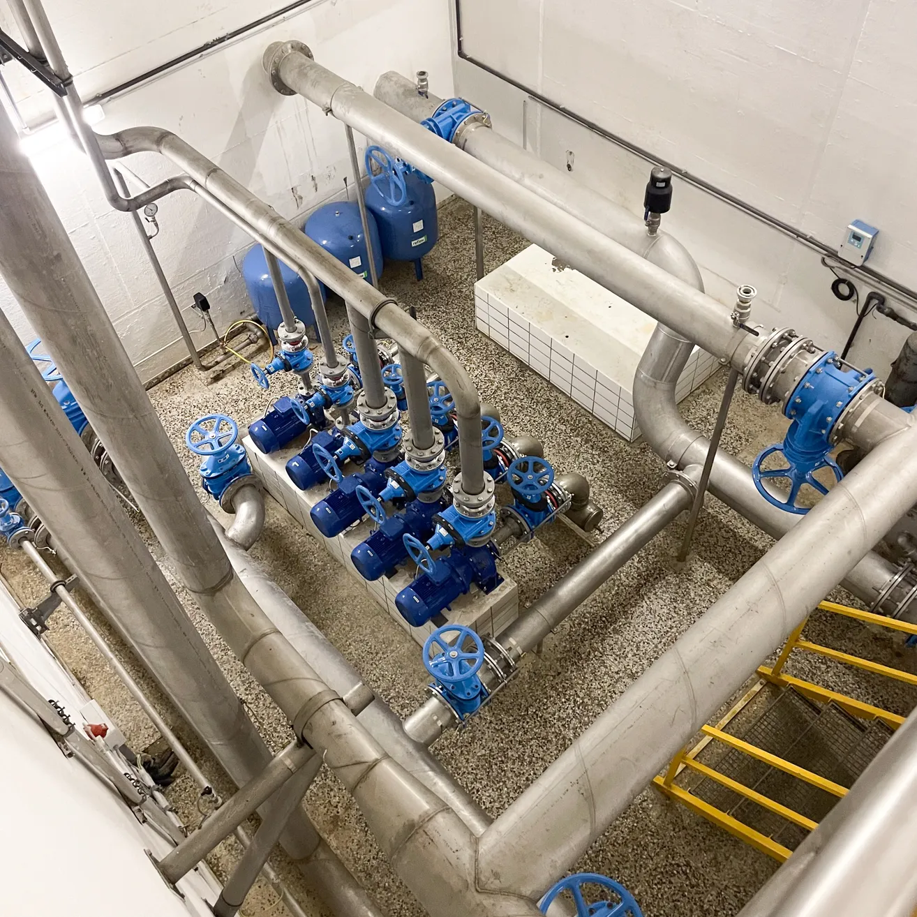 Ein Blick von oben auf eine Industrieanlage mit einem komplexen Netzwerk aus blauen und silbernen Rohren, Ventilen und Tanks.