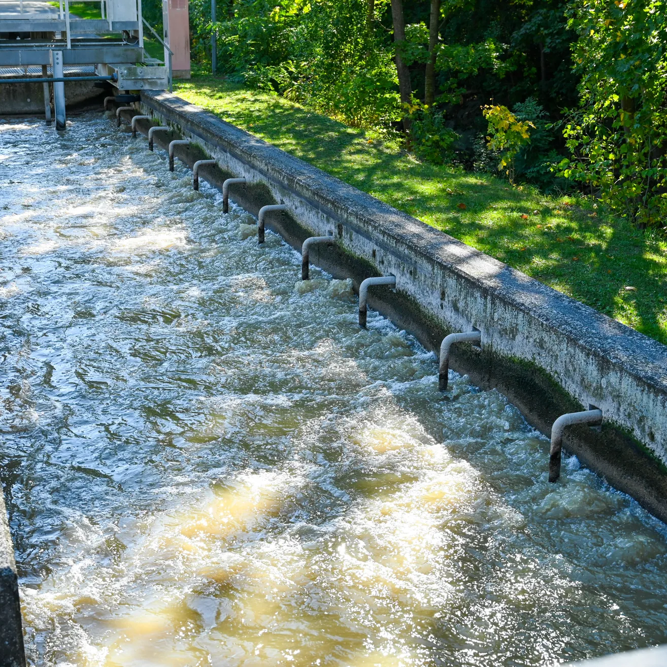 Ein Betonkanal mit fließendem Wasser, umgeben von grünem Gras und Bäumen.