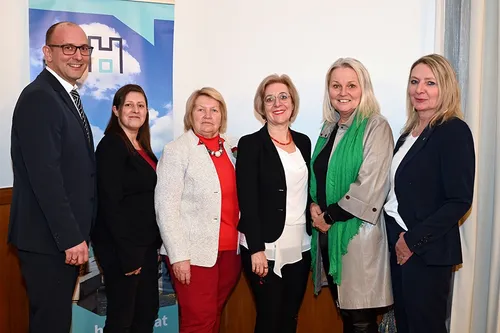 Eine Gruppe von Menschen steht vor einem Banner. Sie lächeln und scheinen für ein Foto zu posieren.