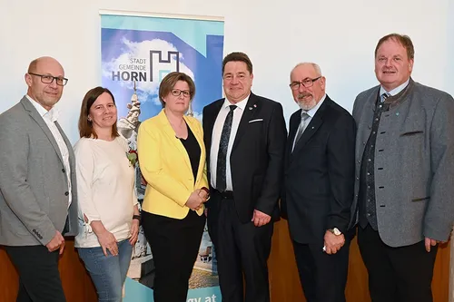 Fünf Personen stehen vor einem Banner mit einer Stadtlandschaft und den Worten Stadt Gemeinde Horn, möglicherweise bei einer Veranstaltung.