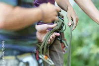 Zwei Personen justieren Kletterseile, wobei eine Person ein Seil mit einem Karabiner hält, während die andere ein Seil mit einem Gurtzeug hält.