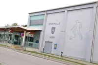 Die Außenseite einer Sporthalle mit den Worten Sporthalle Horn und einem Fußballspieler. Es gibt Treppen, die zum Eingang führen.