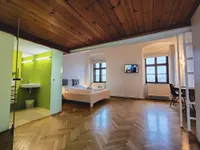 Ein Schlafzimmer mit Holzboden und einem Bett. Der Raum hat eine grüne Wand mit einem Waschbecken und einem Fernseher an der Wand.