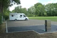 Ein weißer Wohnwagen steht auf einem Parkplatz in der Nähe eines Rasenfeldes. Es gibt eine Ladestation an der Seite.