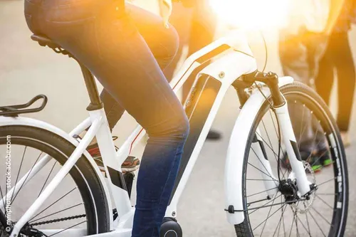 Eine Person fährt an einem sonnigen Tag ein weißes E-Bike, mit verschwommenen Figuren im Hintergrund.