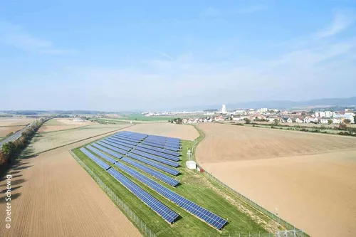 Ein Luftbild einer Solaranlage in einer ländlichen Landschaft mit Feldern und einer kleinen Stadt in der Ferne.