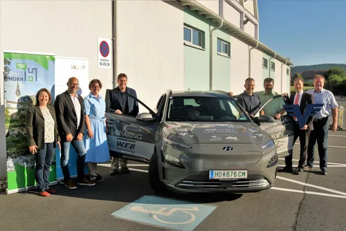 Fünf Personen posieren für ein Foto mit einem grauen Auto. Es handelt sich um einen Hyundai, der die Aufschrift 'car sharing' auf der Seite hat.