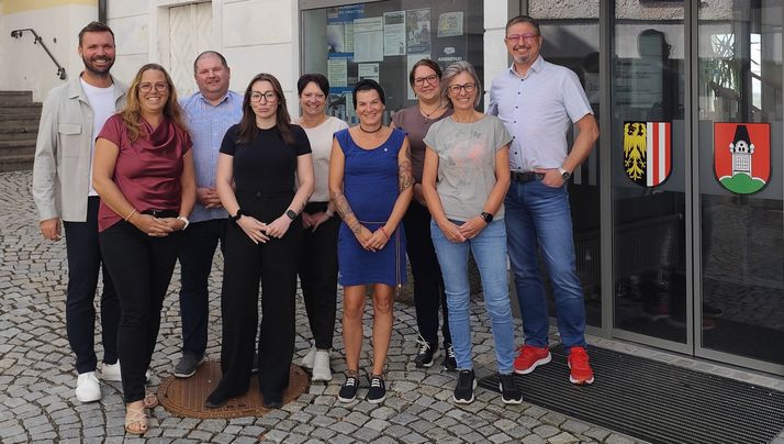 Eine Gruppe von Menschen steht vor einem Gebäude, lächelt und posiert für ein Foto. Sie sind lässig gekleidet und scheinen Kollegen zu sein.