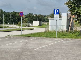 Ein leerer Parkplatz mit einem Parkzeichen und einem Parkverbotsschild. Das Gebiet ist von grünem Gras und Bäumen umgeben.