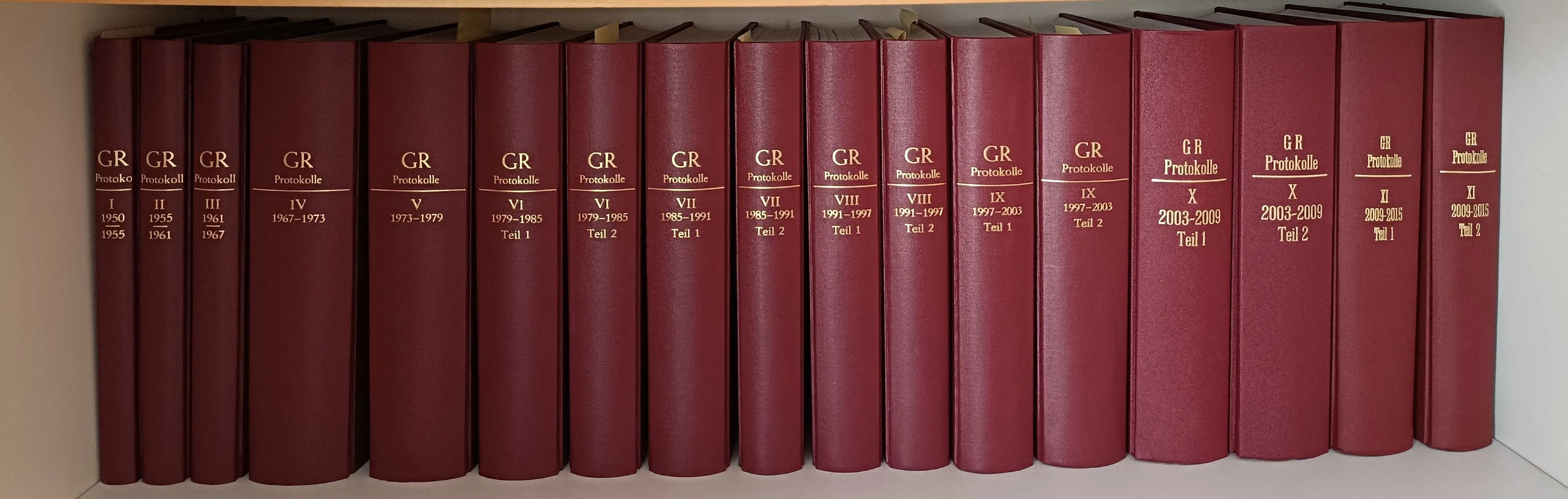 Eine Reihe roter Bücher mit der Aufschrift 'Protokolle' ist ausgestellt. Sie sind von VI bis IX nummeriert, wobei die Bandnummern von 1979 bis 2003 reichen. Jedes Buch hat eine unterschiedliche Band- und Teilnummer.