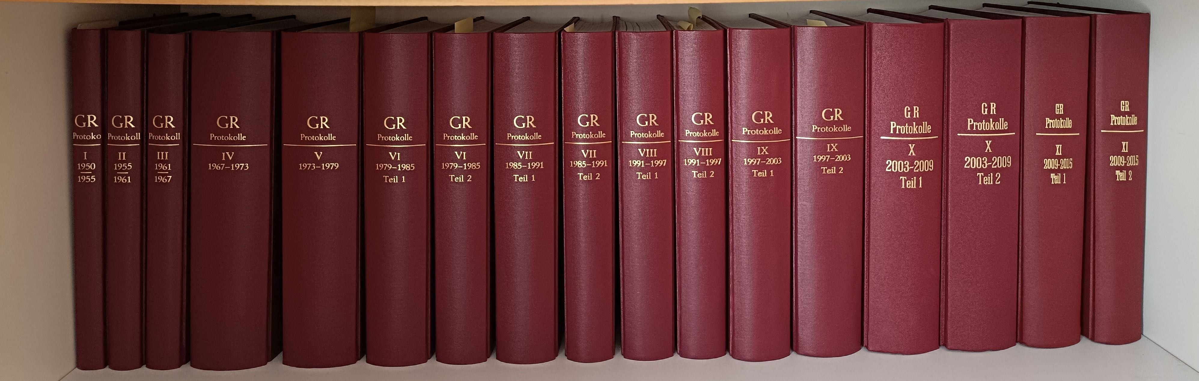 Eine Reihe roter Bücher mit der Aufschrift 'Protokolle' ist ausgestellt. Sie sind von VI bis IX nummeriert, wobei die Bandnummern von 1979 bis 2003 reichen. Jedes Buch hat eine unterschiedliche Band- und Teilnummer.