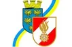 Das Bild zeigt ein Wappen mit einem blauen Schild, der einen goldenen Adler und eine goldene Burg oben darauf hat, begleitet von einem roten und weißen Schild mit einem Feuer- und Zahnradsymbol.