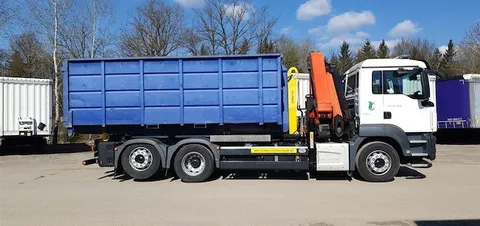 Ein blauer und weißer Sattelschlepper mit einem blauen Müllcontainer am Heck steht auf einem Parkplatz.