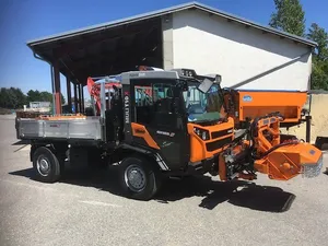 Ein orange-schwarzes Nutzfahrzeug steht vor einem Gebäude mit Metalldach.