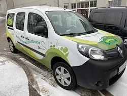 Ein weiß-grüner Renault Kangoo Van, der vor einem Gebäude auf einer verschneiten Straße geparkt ist.