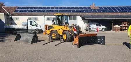 Ein gelbes Baufahrzeug ist vor einem Gebäude mit Solarpanelen auf dem Dach geparkt.