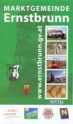Ein grünes Plakat, das die Marktgemeinde Ernstbrunn bewirbt, mit einer Collage von Bildern, darunter ein Zug, eine Kuh und ein Feld, und einer Website-Adresse am unteren Rand.