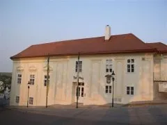 Ein großes weißes Gebäude mit einem roten Dach und mehreren Fenstern, das auf einer Straße mit Fahnen davor steht.